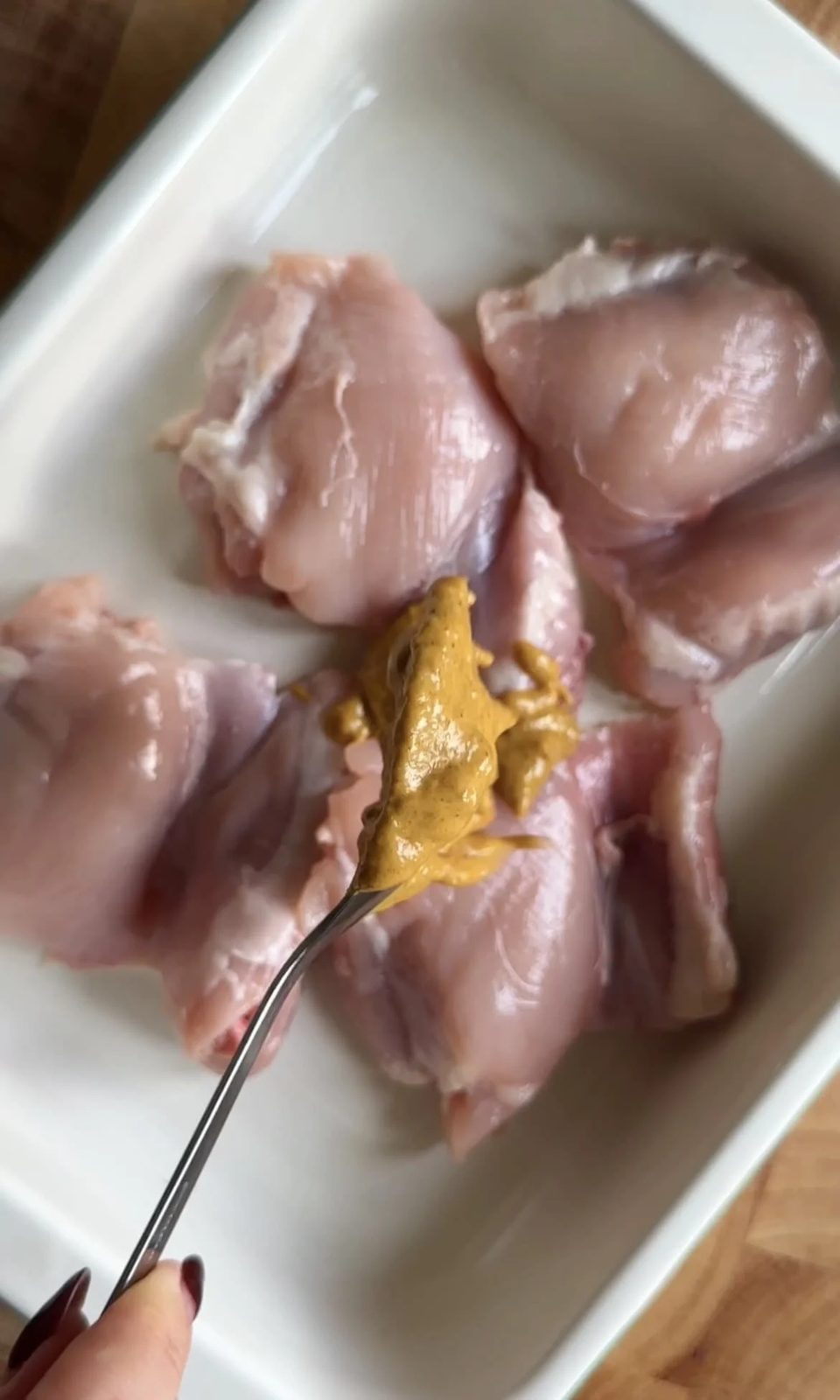 Placing satay sauce over chicken thighs in baking dish.