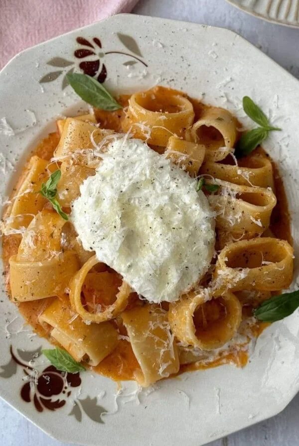a white bowl filled with tomato butter pasta and topped with burrata.