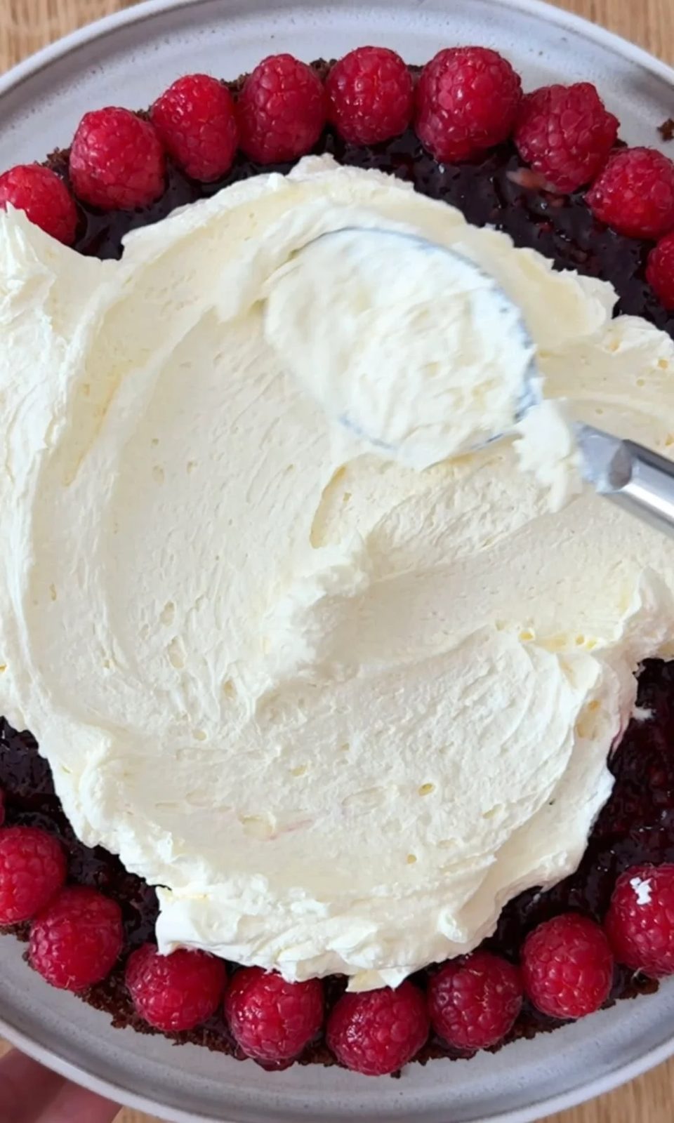 adding whipped cream to the chocolate raspberry cake.