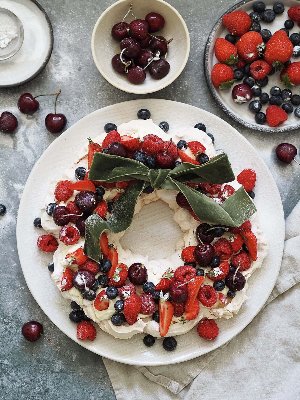 Christmas Pavlova on a plate with bowls of berries.
