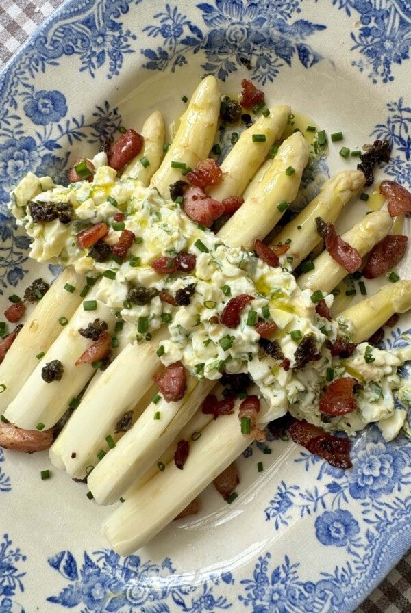 white asparagus topped with bacon on blue and white plate