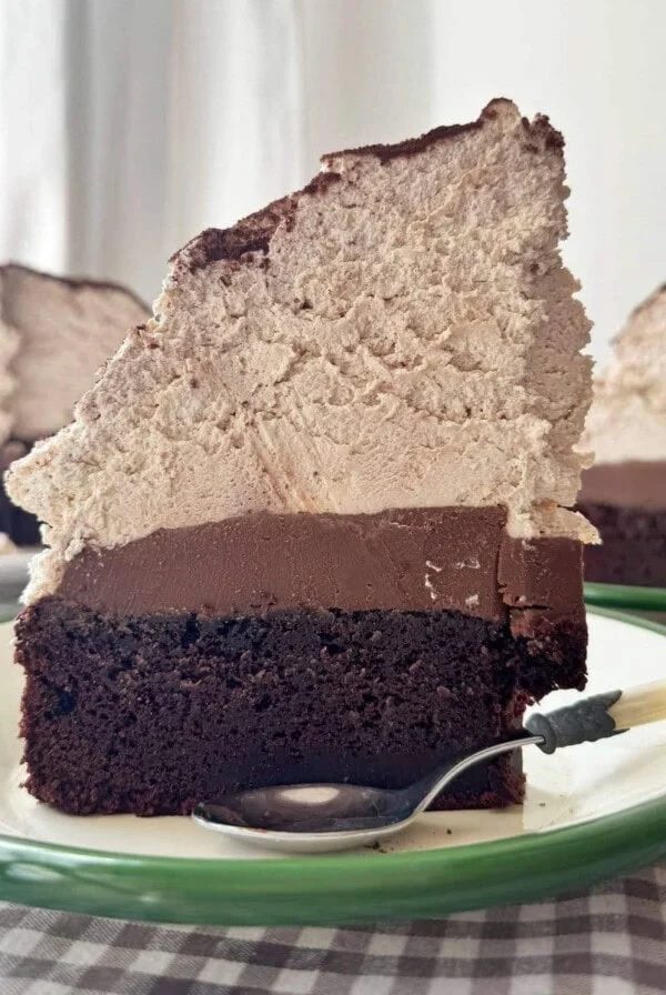 slice of chocolate mud cake with malted whipped cream stood on a green plate.