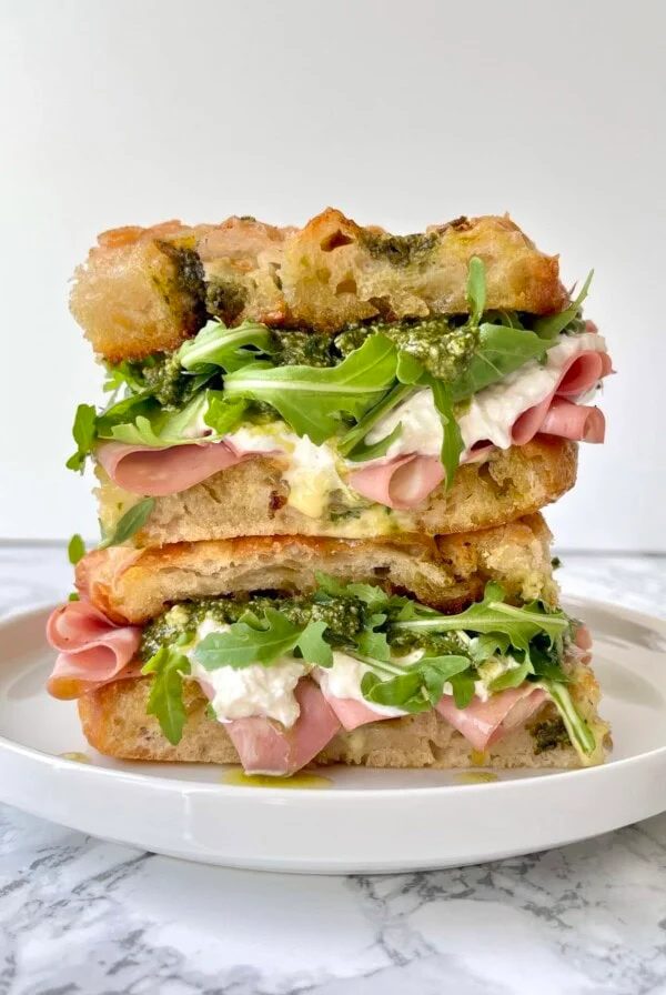 mortadella burrata sandwich with rocket, pesto, stacked on a plate