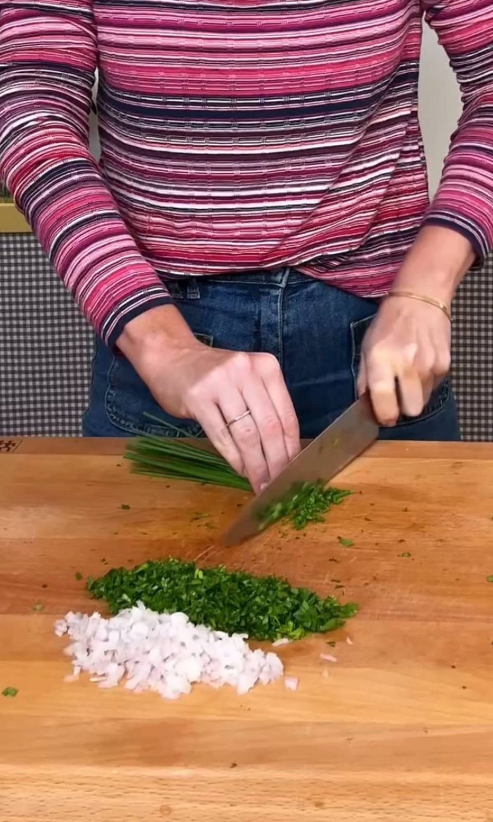 Chopping chives and other herbs with shallots on cutting board.