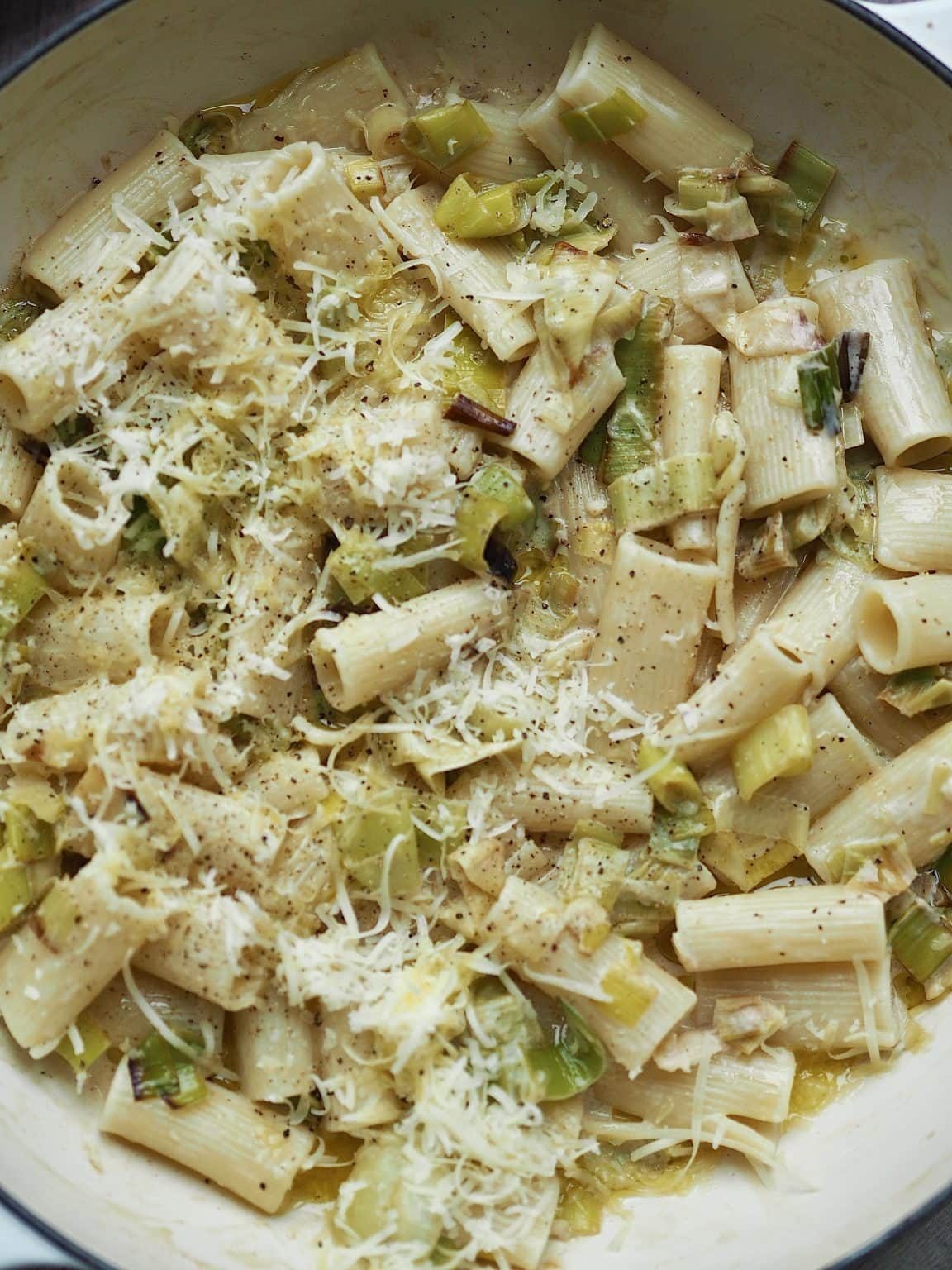 Close up of creamy leek rigatoni in a shallow casserole topped with grated cheese.