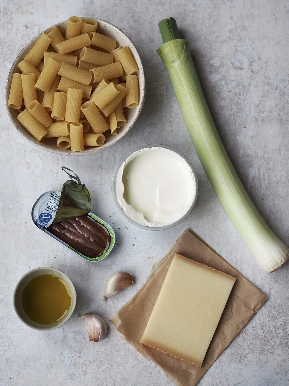 Ingredients to make Creamy Caramelized Leek Pasta with Gruyere on a grey background.