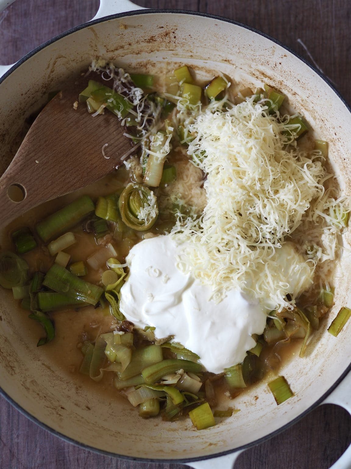 Grated cheese and creme fraiche being stirred into slow cooked leeks.