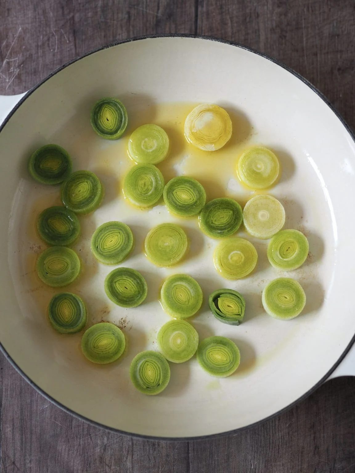 Uncooked leeks in olive oil in a white shallow casserole.