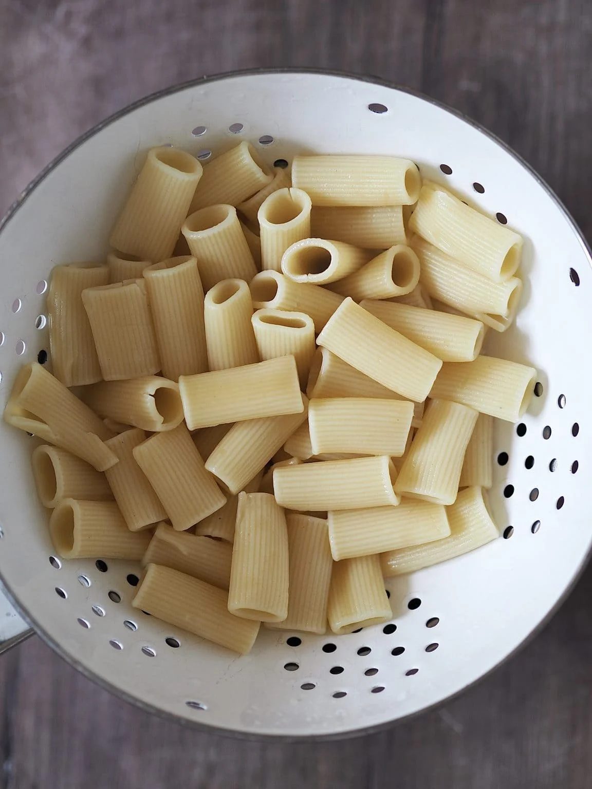 Freshly cooked rigatoni pasta in a white colander.
