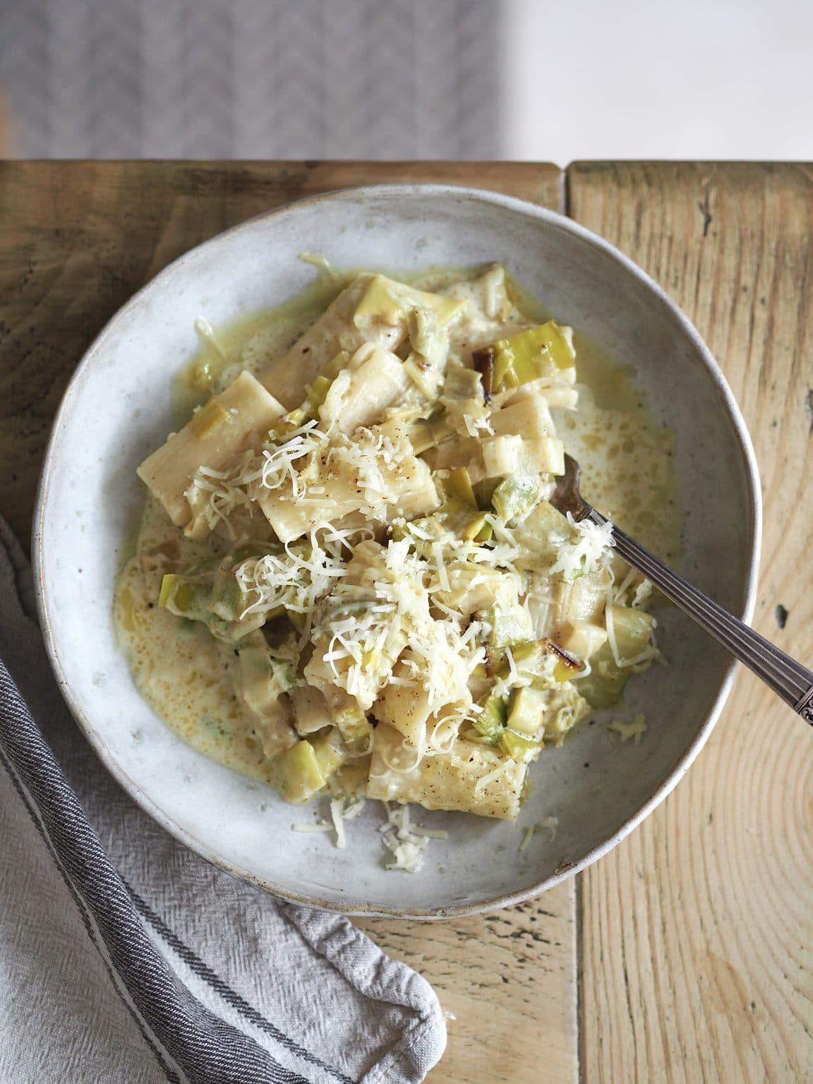Stone bowl of creamy leek pasta topped with grated cheese.