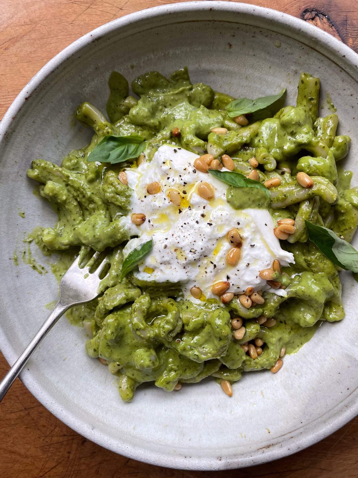 Stone bowl of pesto pasta sauce with burrata and toasted pine nuts.