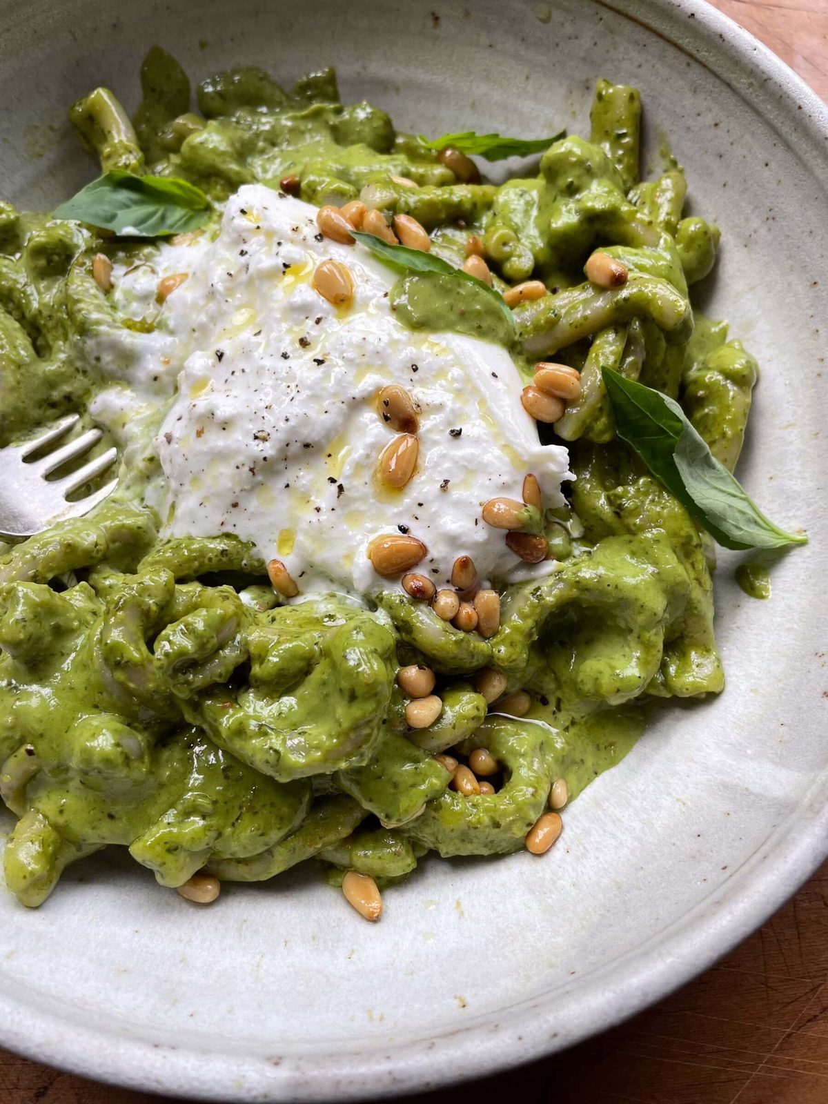 Close up of a bowl of creamy pesto pasta sauce topped with toasted pine nuts.