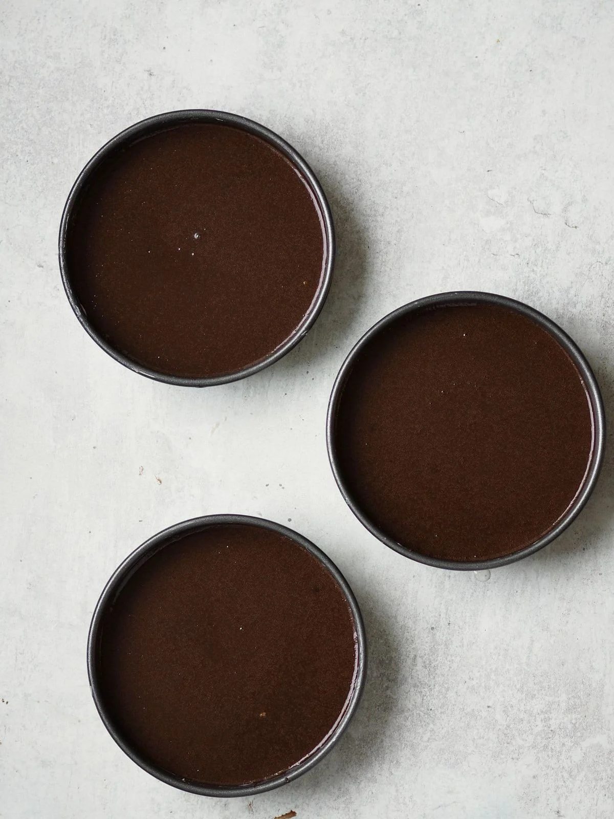 Chocolate cake batter in three round cake pans
