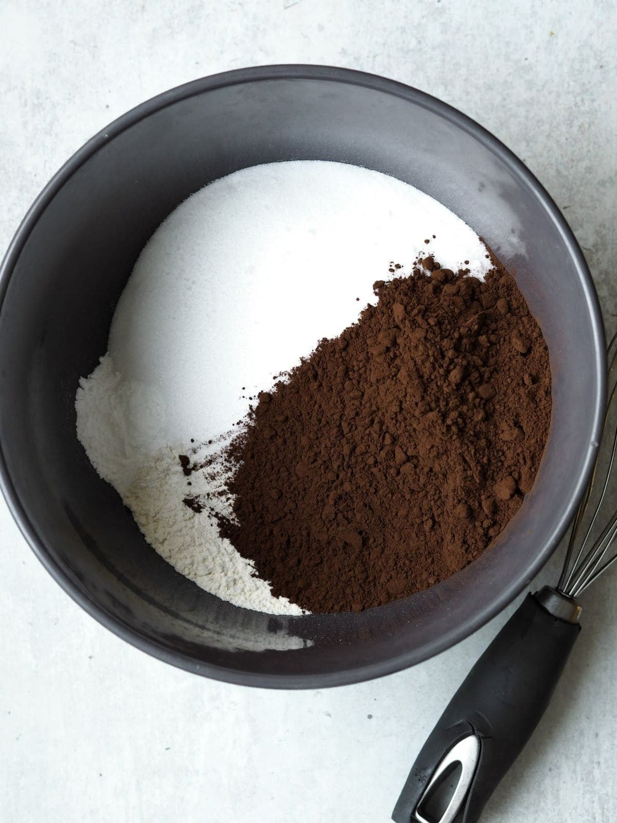 Adding cocoa powder to sugar in bowl.