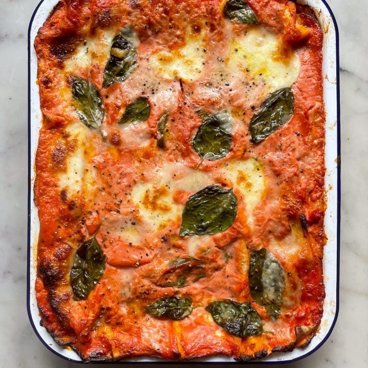 Baked courgette lasagne (zucchini lasagna) in a falconware baking dish topped with basil leaves.
