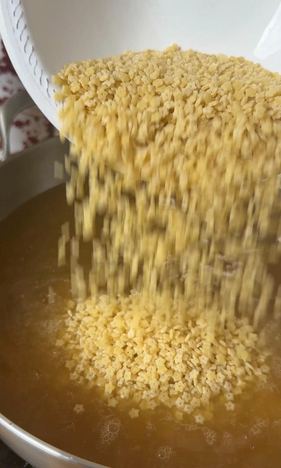 Pouring pastina into chicken stock.