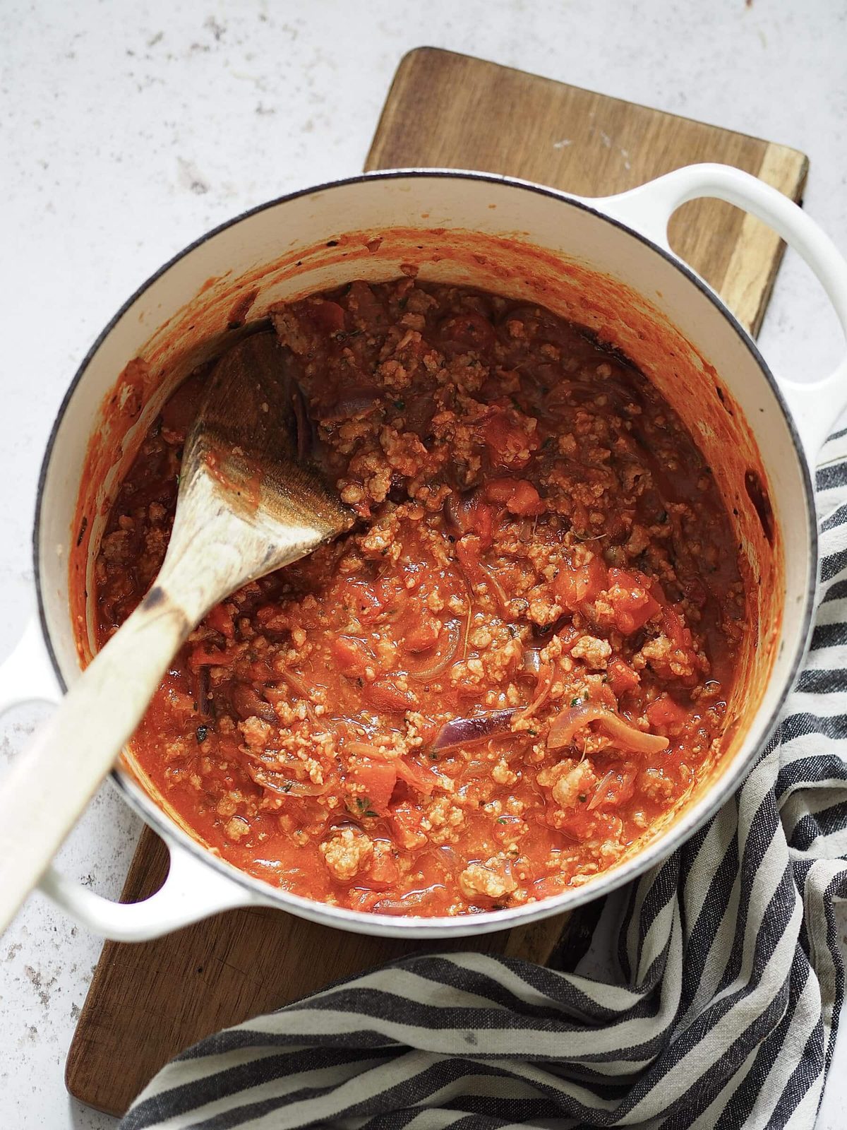 Sausage ragu being stirred in a white casserole dish with a wooden spoon.
