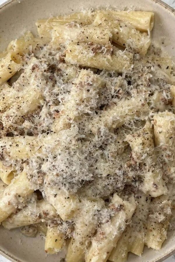 creamy sausage pasta in a beige bowl covered in a grating of cheese