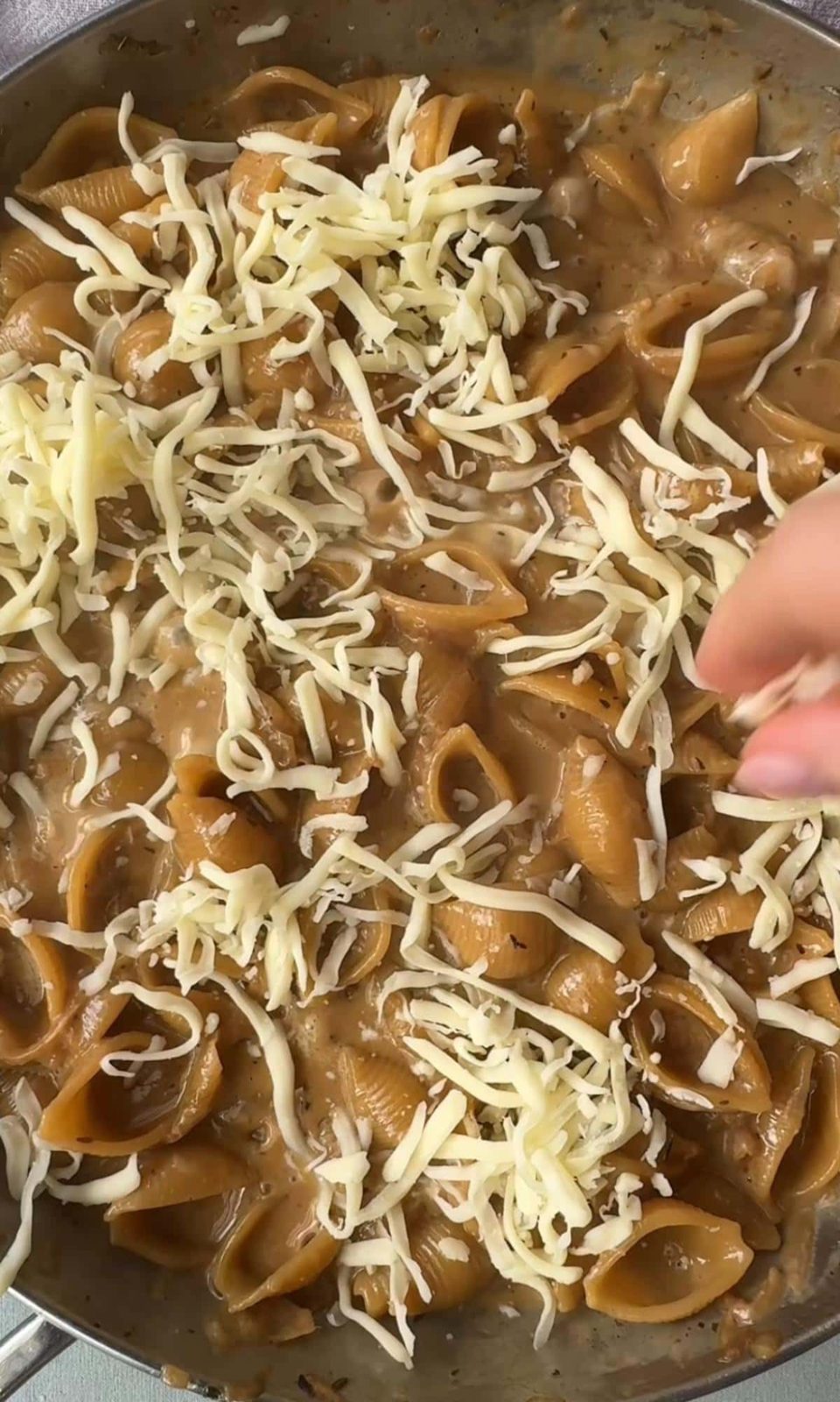Adding gruyere to pan with French onion soup pasta.