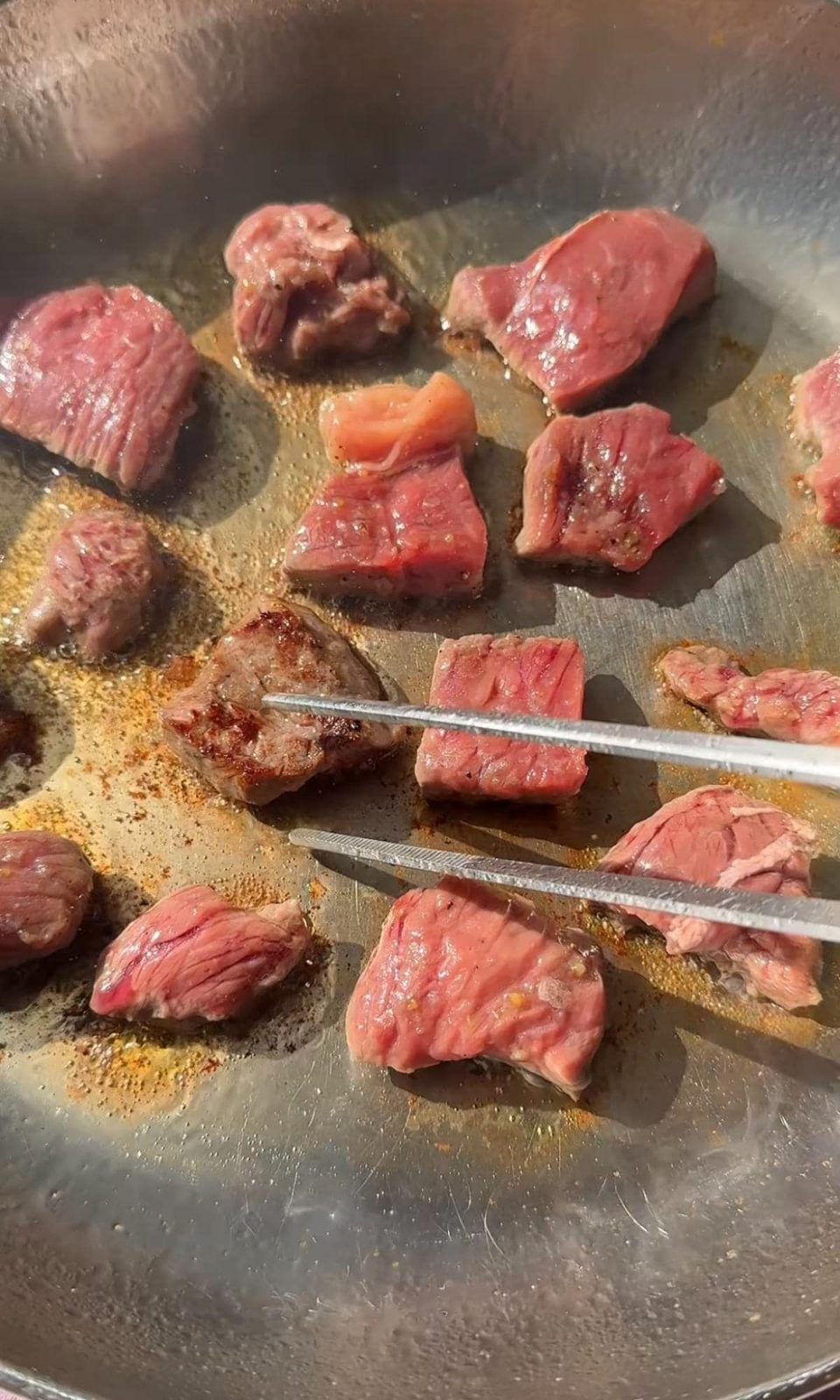 Frying seasoned steak bites in pan.