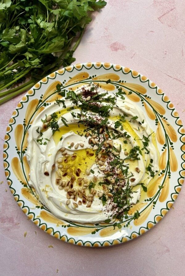 garlic labneh with pine nuts and parsley on a yellow and green plate