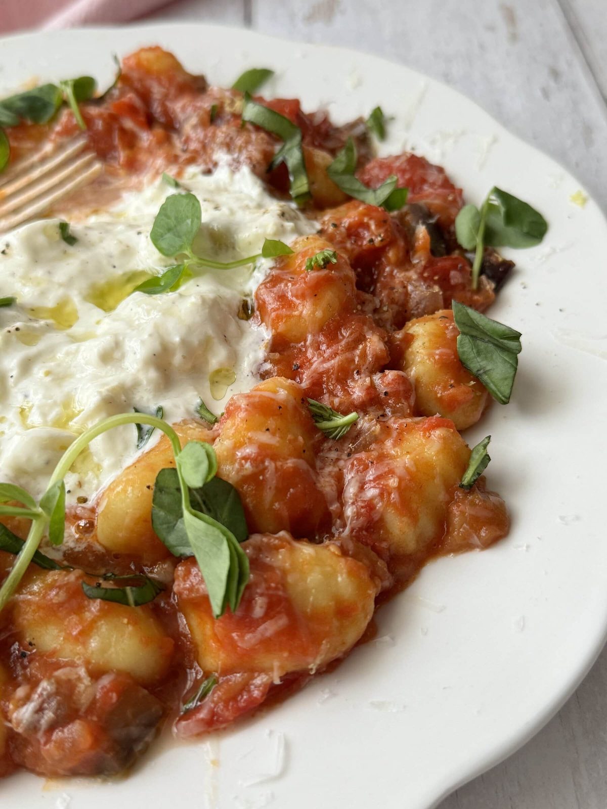 gnocchi alla norma on a white plate with burrata and fresh basil on top.