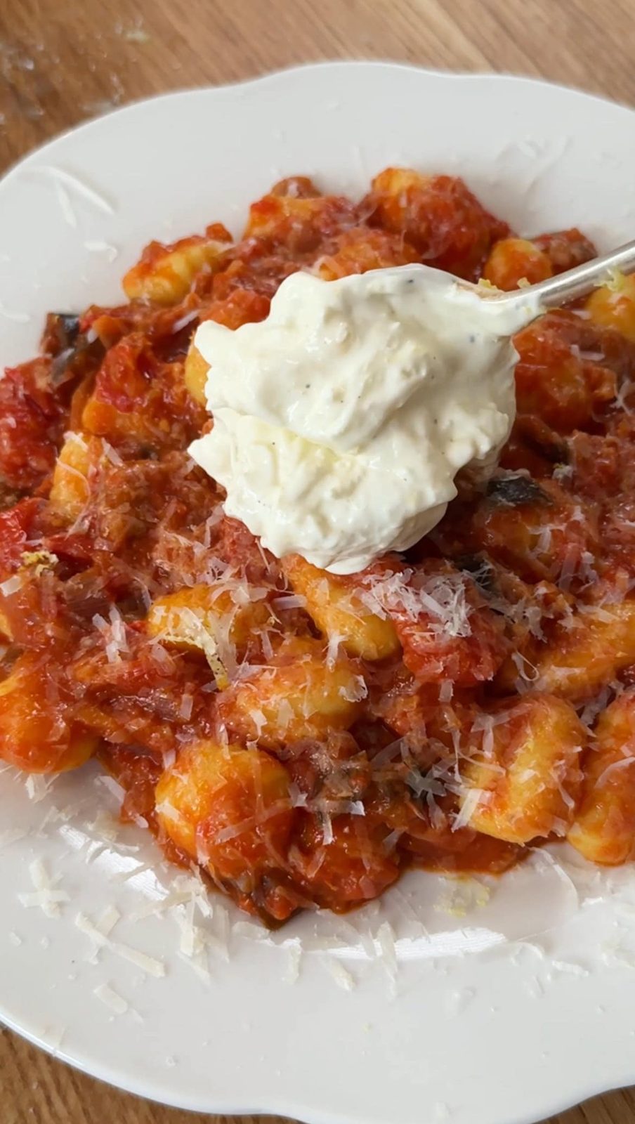 adding creamy topping to gnocchi alla norma.