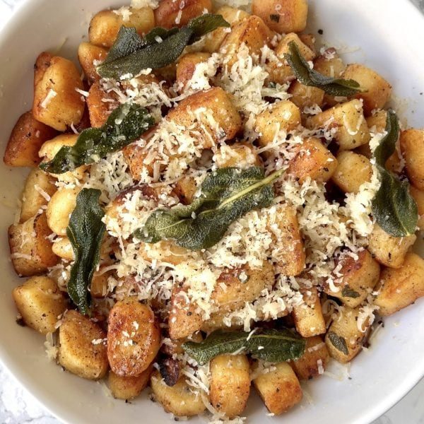 White bowl of crispy gnocchi with parmesan and sage.
