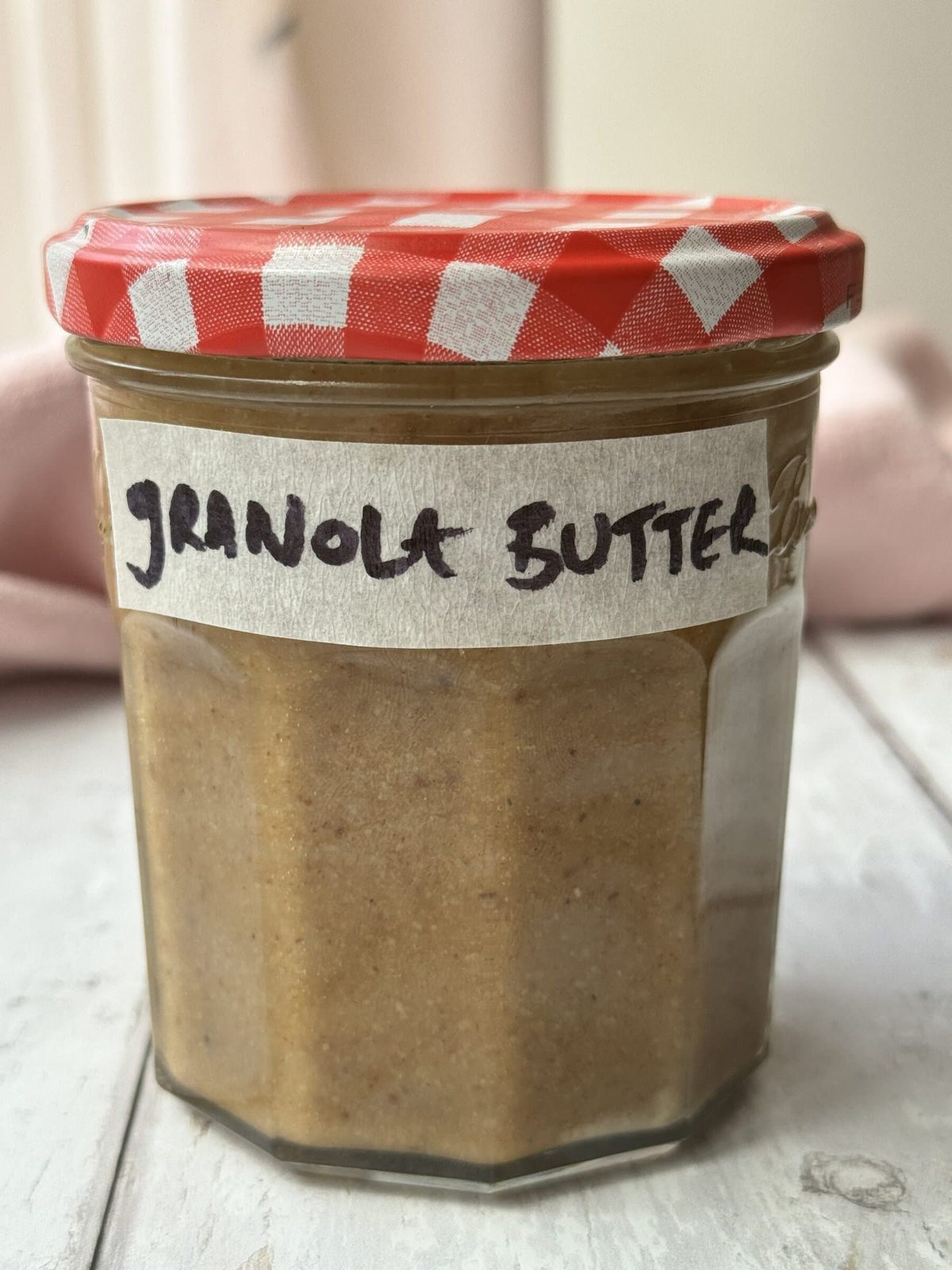 a jar of granola butter with a gingham lid and a label that reads granola butter.