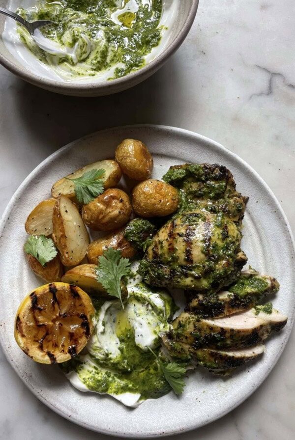 Zingy Grilled Chimichurri Chicken with Roasted Potatoes on a grey plate with a bowl of chimichurri yoghurt behind