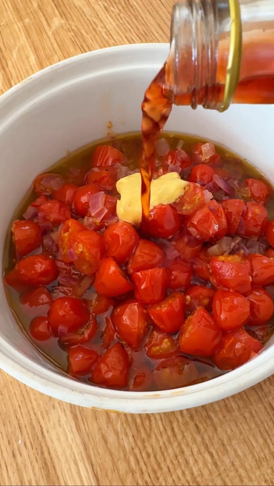Pouring red wine vinegar into bowl with roasted tomatoes and veggies.