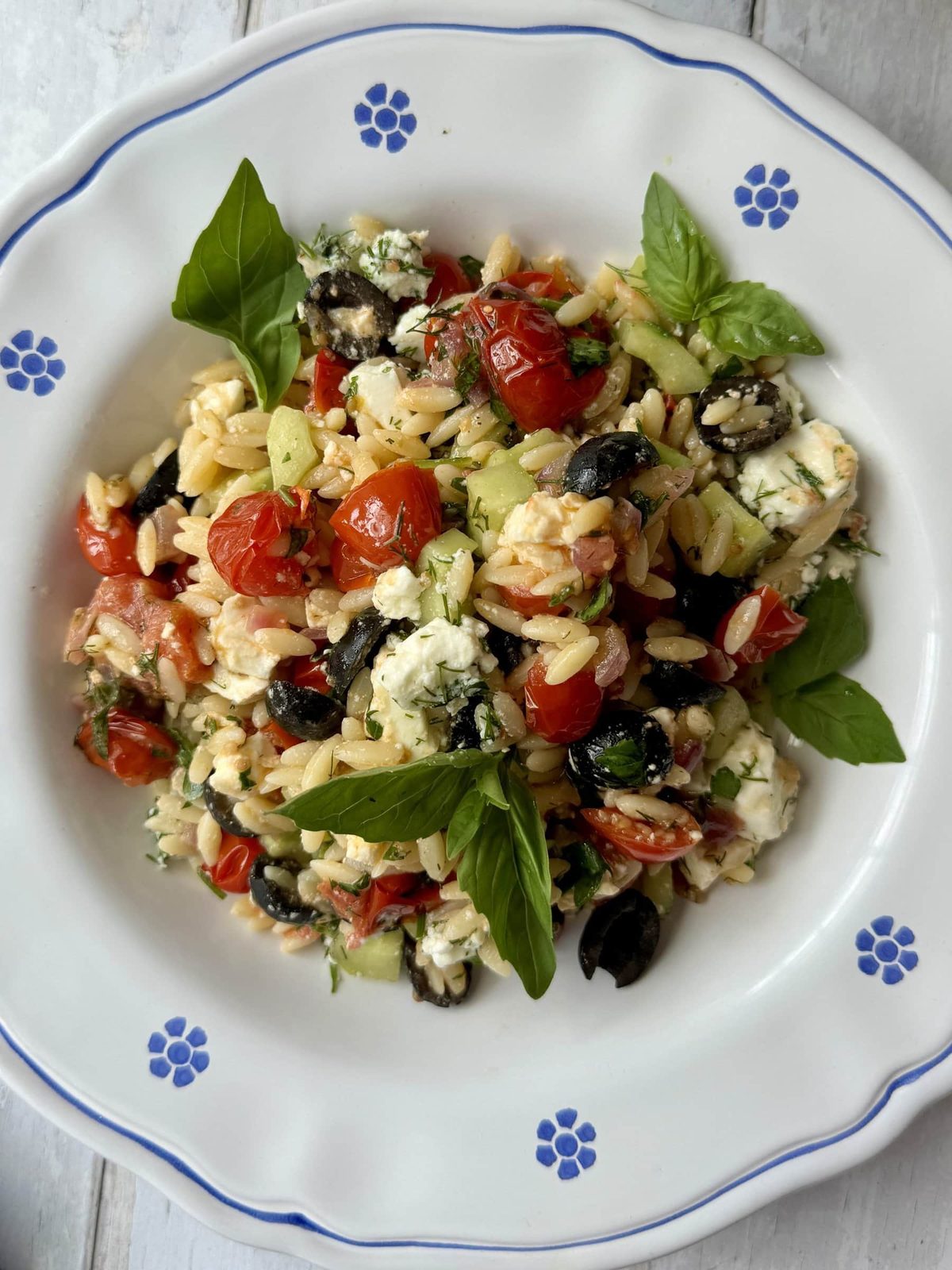 Greek pasta salad with orzo, feta, tomatoes, and herbs in white bowl with blue flowers.