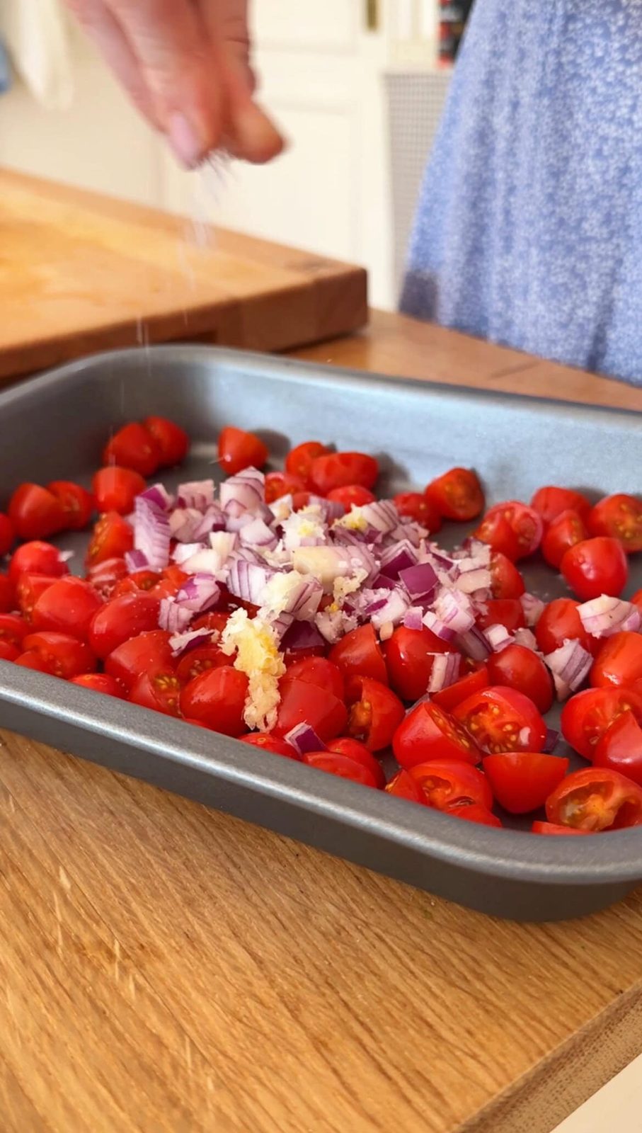 Sprinkling salt over tomatoes, onions, and garlic in baking pan.