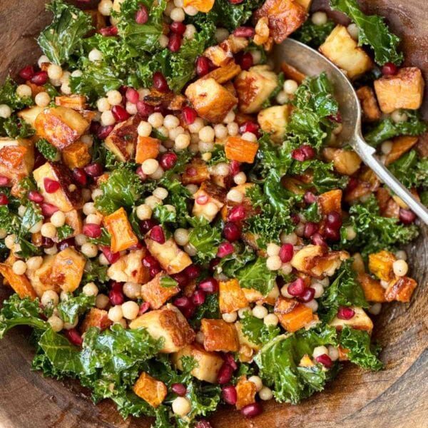 halloumi salad with kale and pomegranate in a wooden bowl.