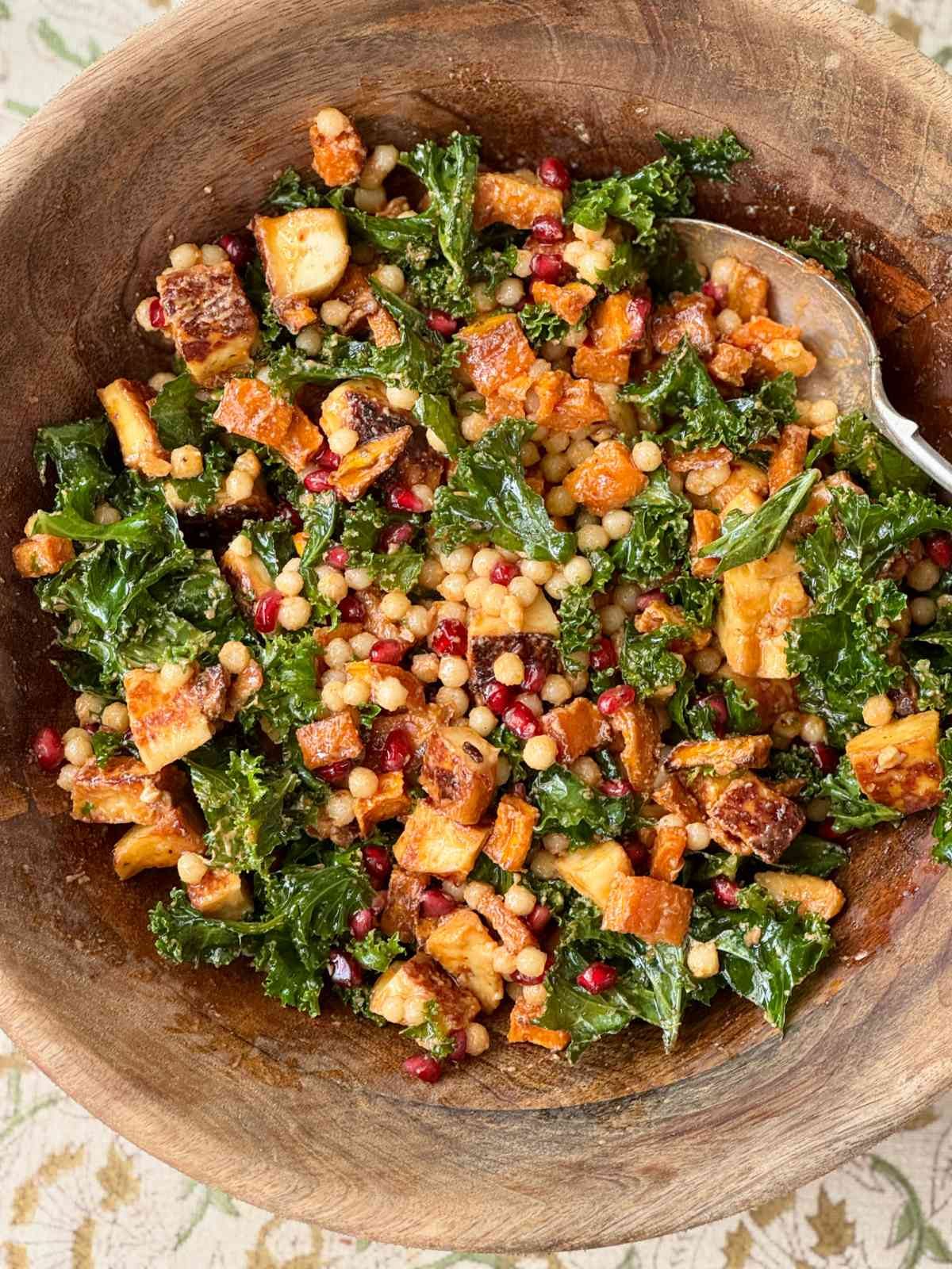 halloumi salad with kale and pomegranate in a wooden bowl.