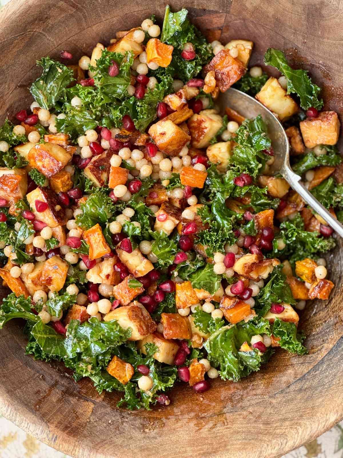 halloumi salad with kale and pomegranate in a wooden bowl.