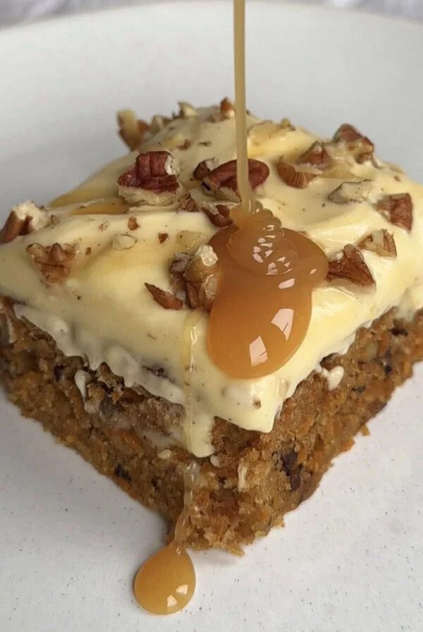 drizzling caramel sauce on a slice of carrot cake tray bake.