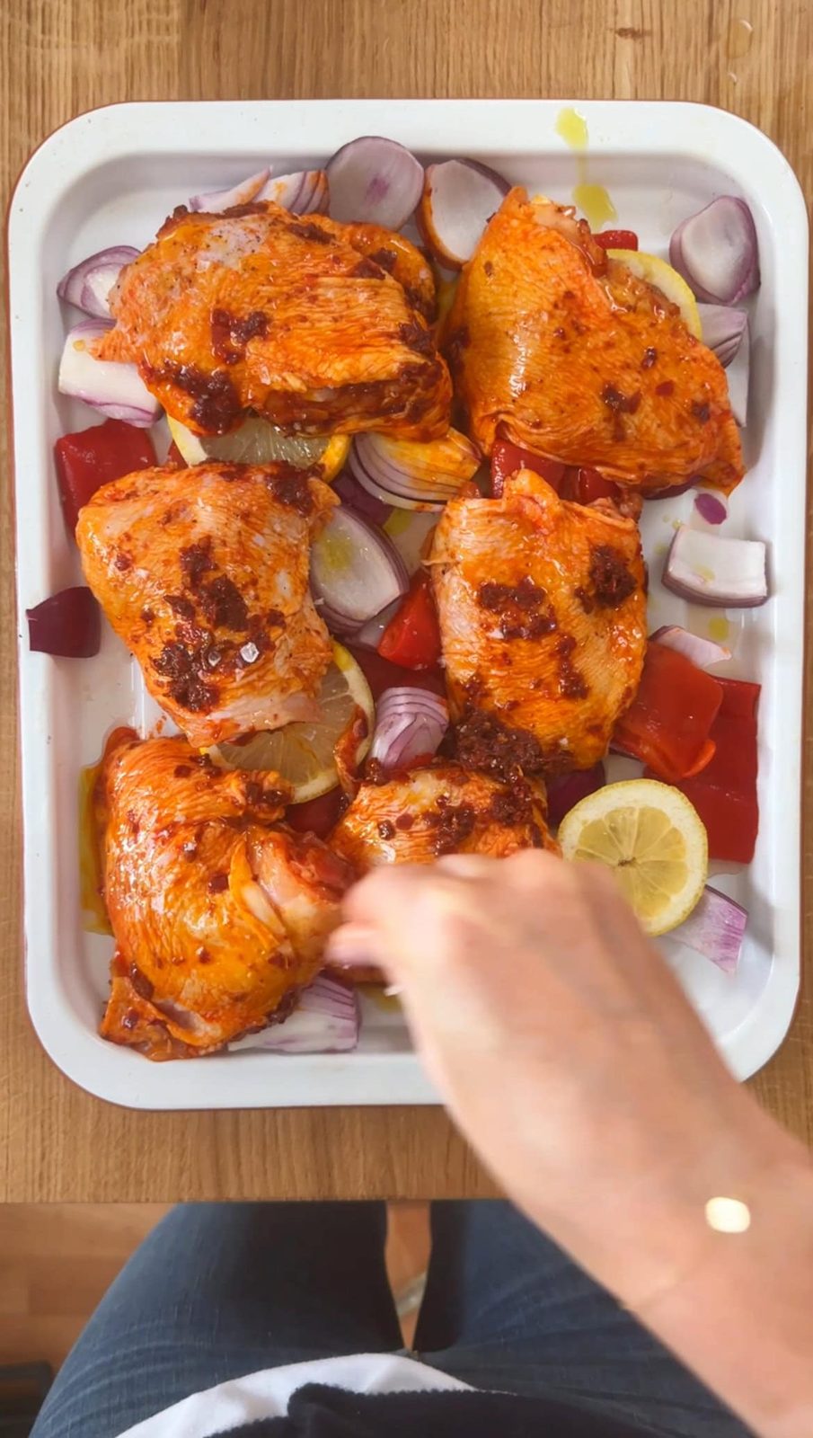 Sprinkling salt over harissa chicken with peppers, onions, and lemons in pan.