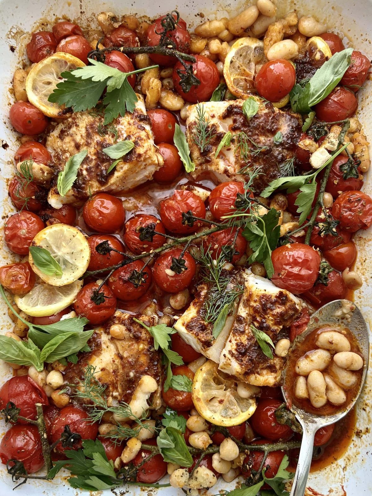 Spooning beans from a harissa cod and cherry tomato traybake.