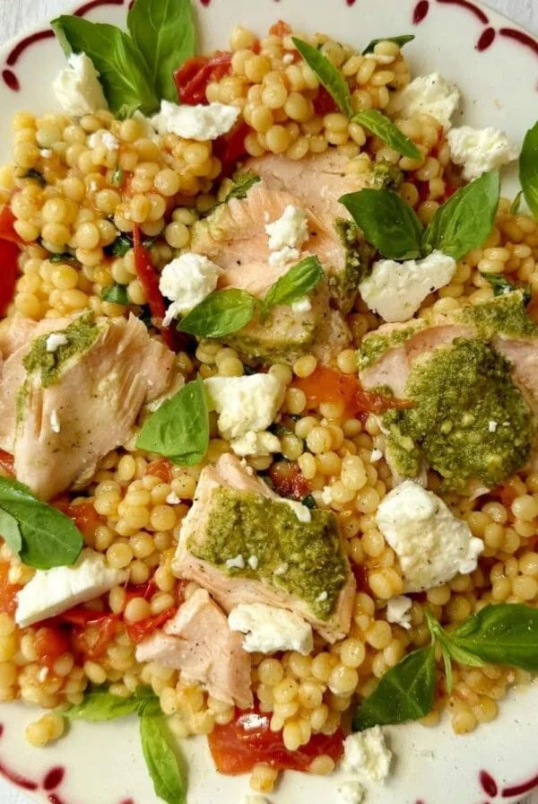 salmon with pesto crust and roasted tomato giant couscous salad on a plate.