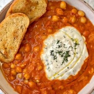 Tomato and chickpea stew in bowl with sliced bread.