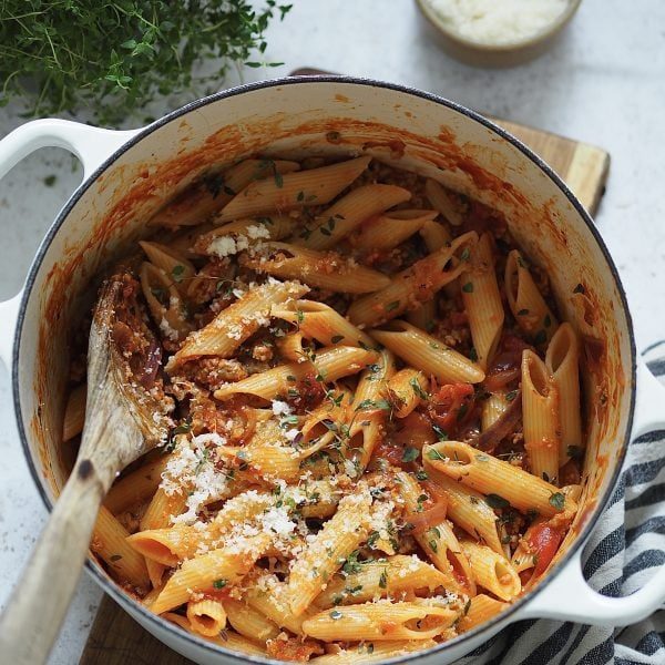 Penne with sausage ragu and grated cheese in a white casserole dish.