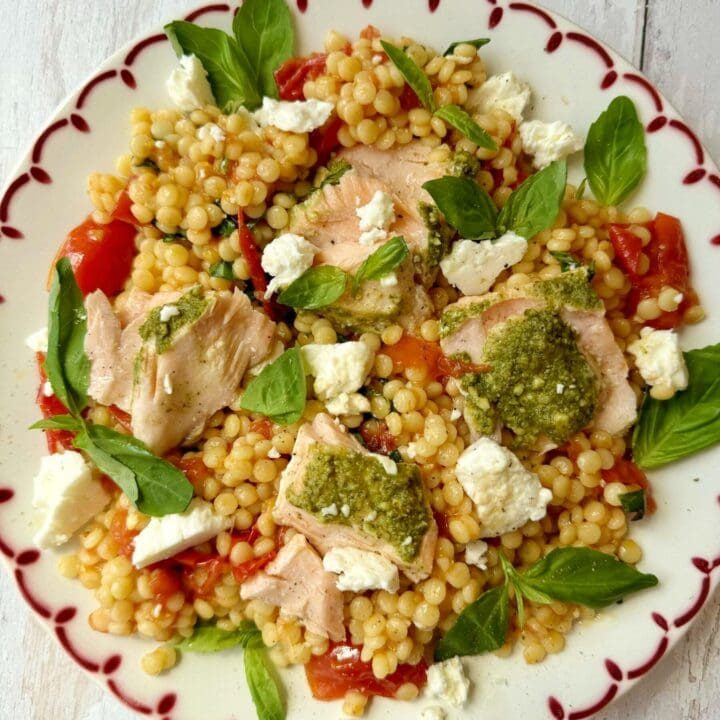 salmon with pesto crust and roasted tomato giant couscous salad on a plate.
