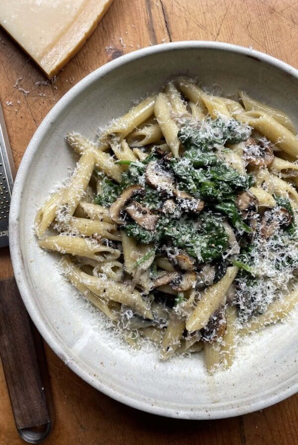 creamy mushroom and spinach pasta in a grey bowl with parmesan rind next to the bowl.