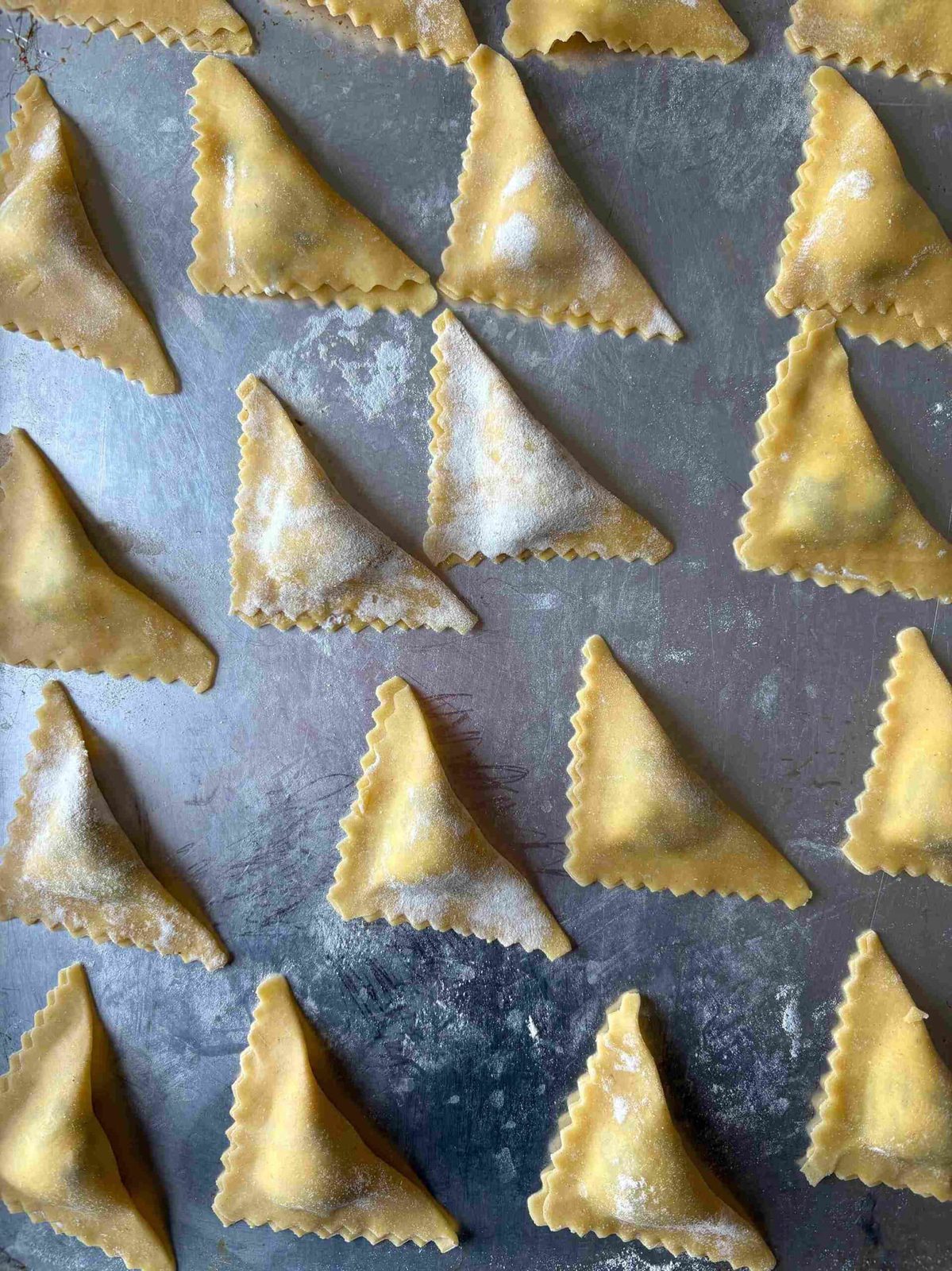 Uncooked triangoli pasta on baking sheets.