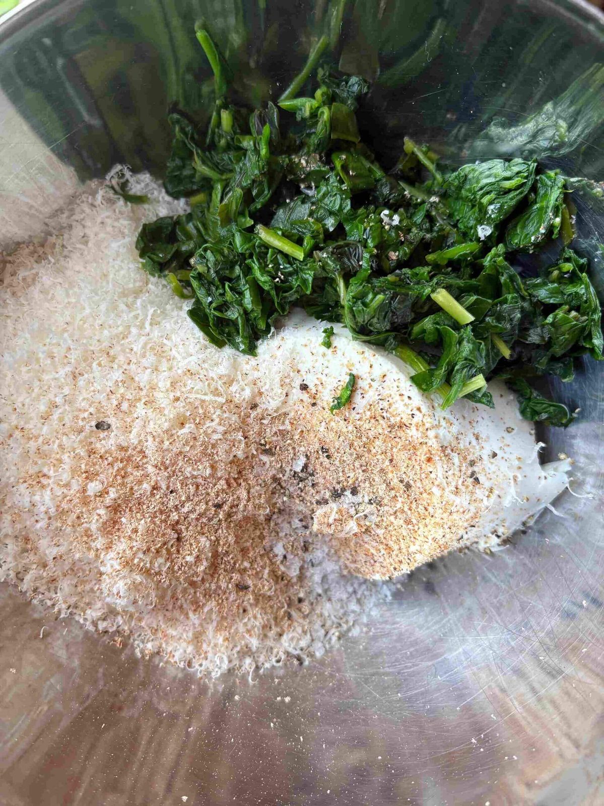 Spinach and ricotta with seasonings in glass bowl.