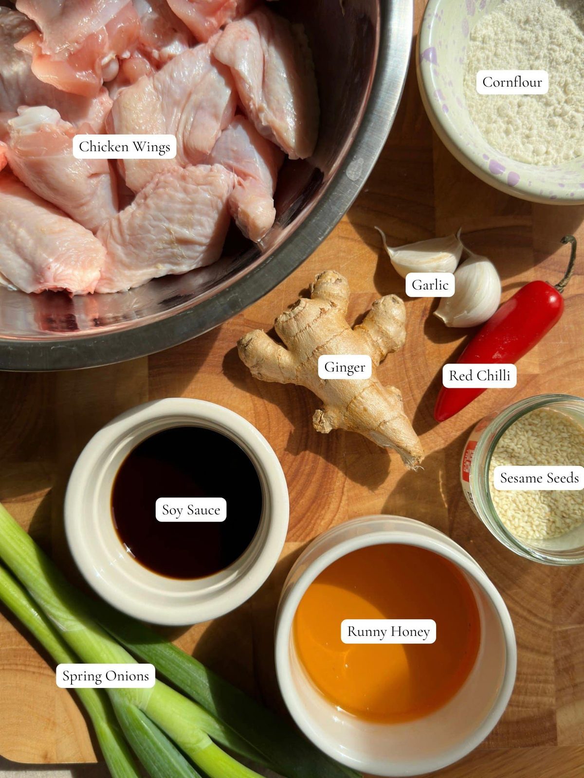 Raw chicken, ginger, scallions, chili, honey, sesame seeds, and other ingredients on table.