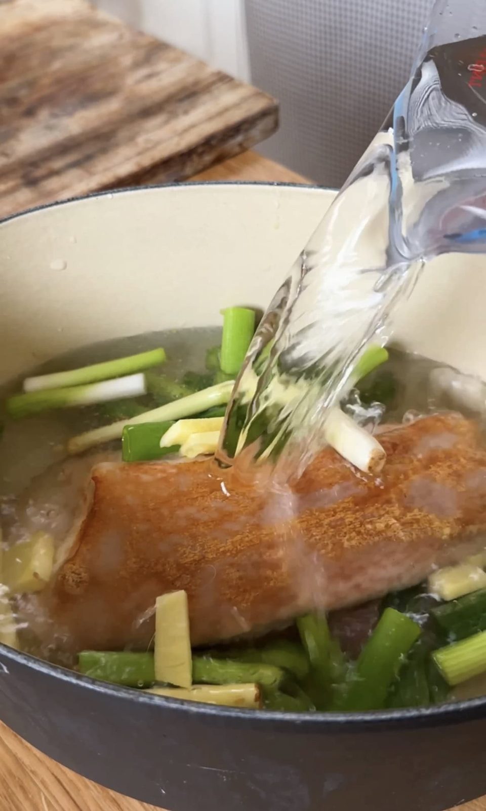 Pouring water over pork belly and veggies.