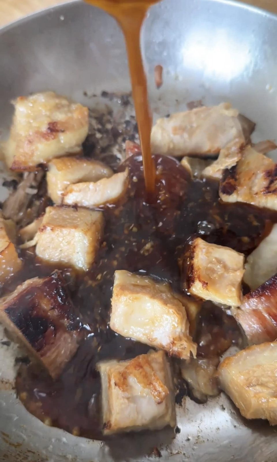 Pouring sticky sauce over the pork belly chunks.