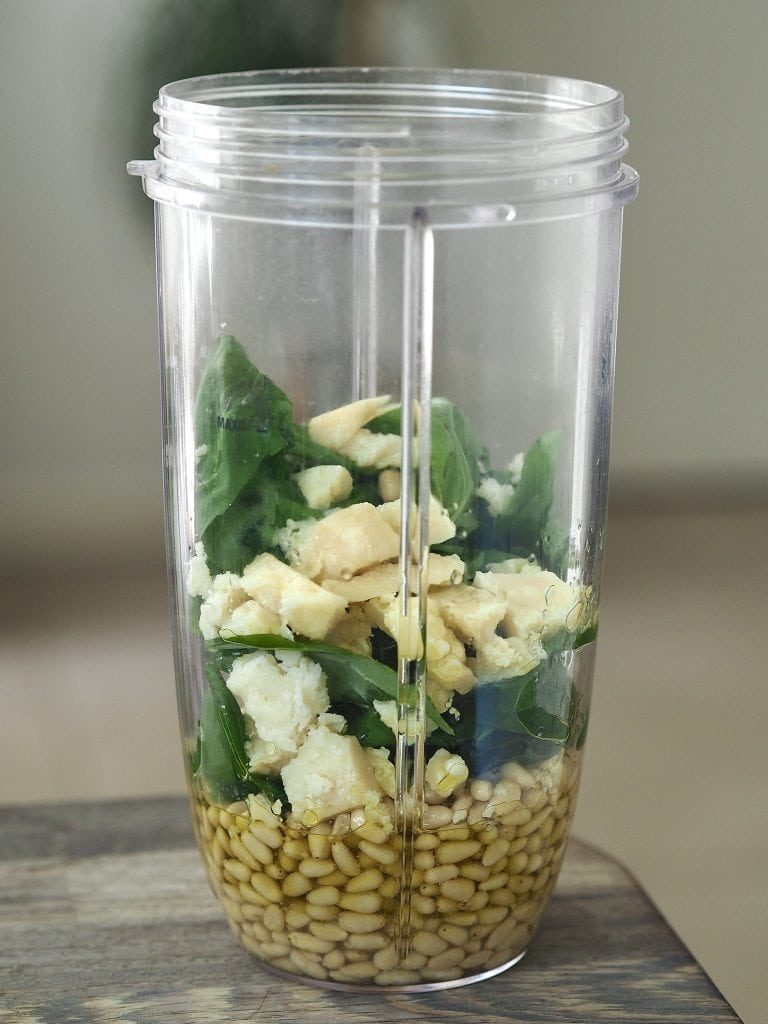 Pesto ingredients in the body of a bullet blender.